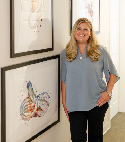 Andrea Wagner of Advanced Hearing Care standing in the hallway of the practice next to pictures ear-based art